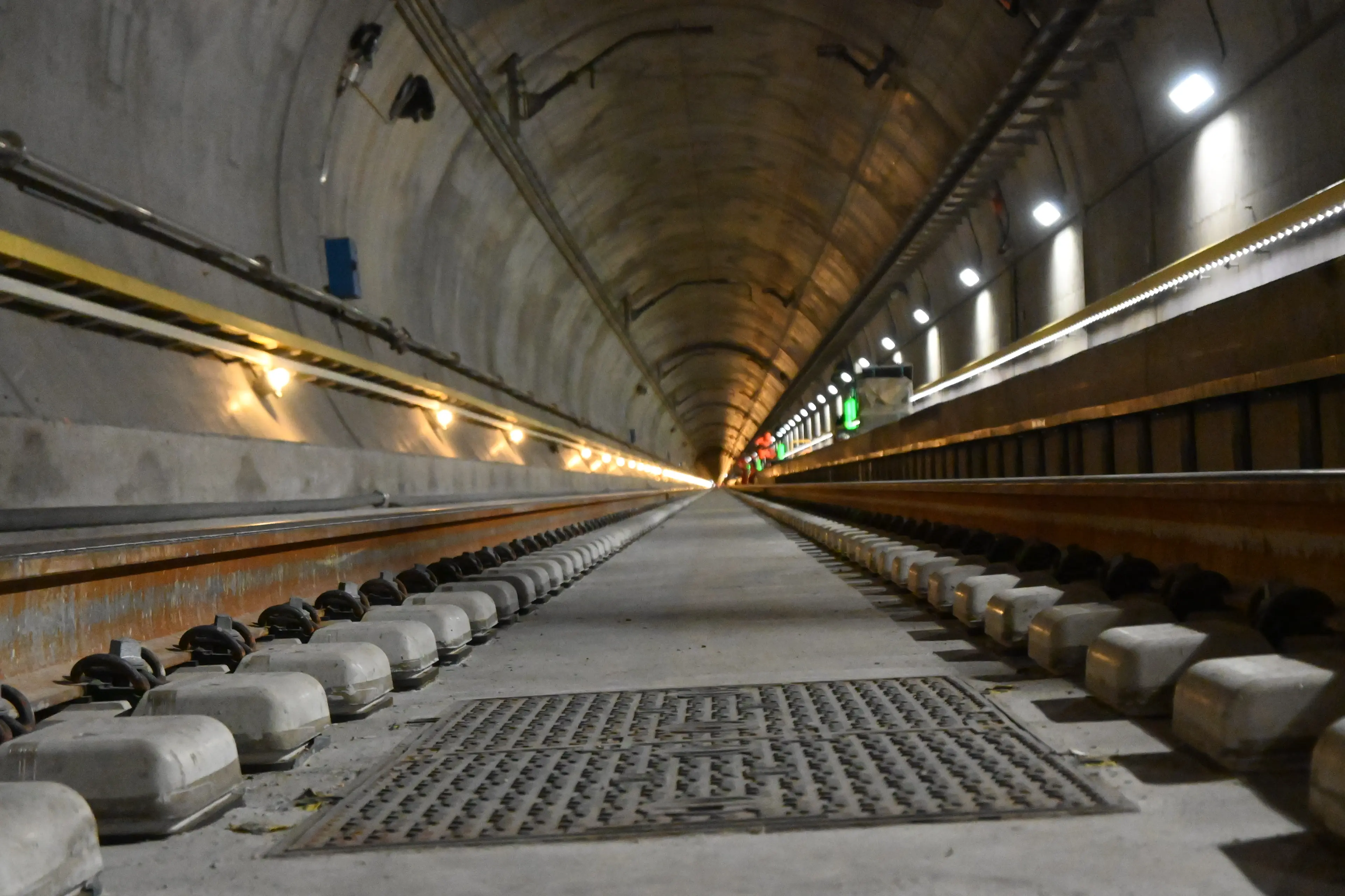 Interior view of a long underground railway tunnel with two tracks, concrete walls, and lights lining the sides.