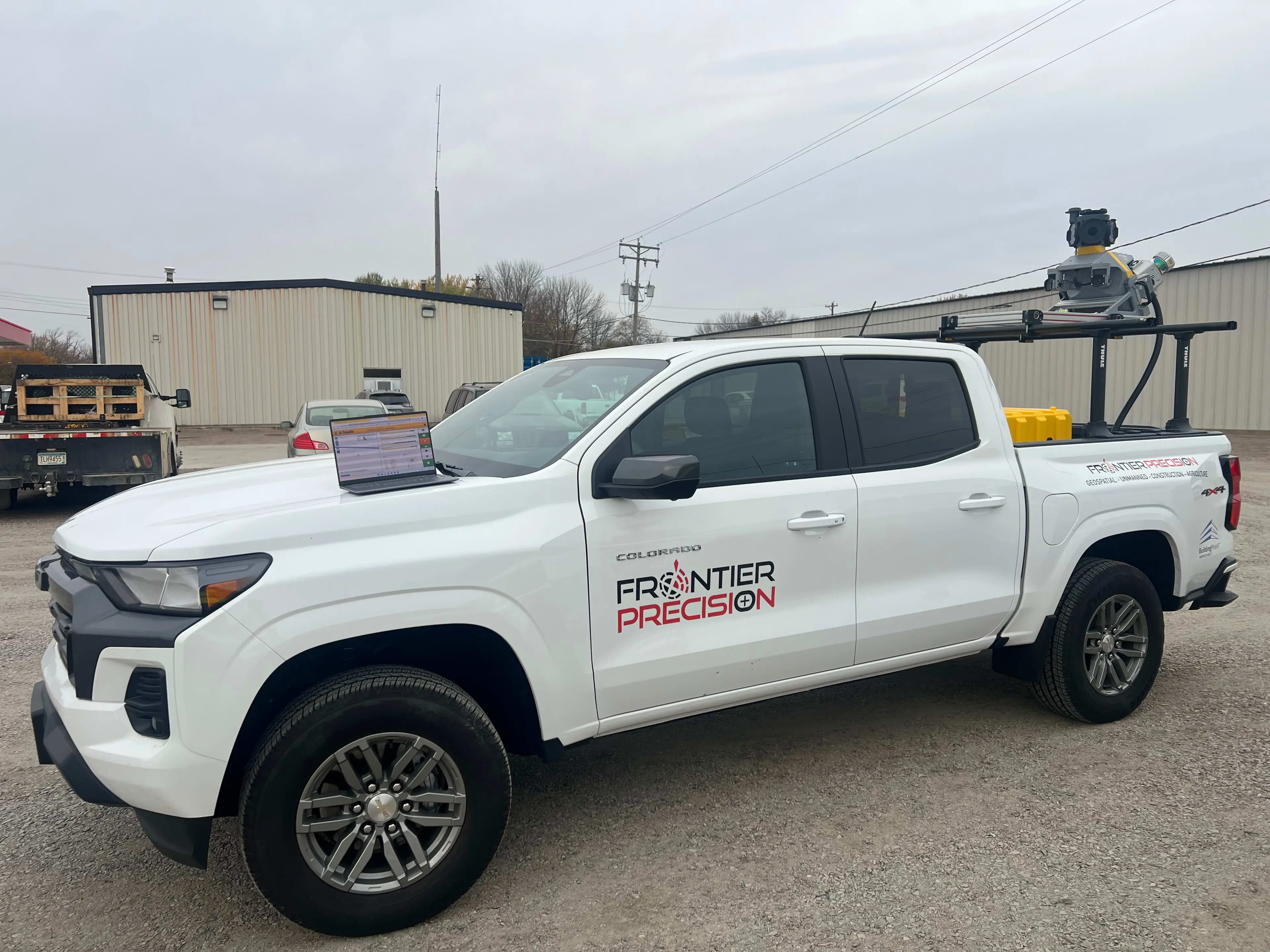 White Chevrolet Colorado truck branded with Frontier Precision logo, equipped with survey equipment on roof rack and a laptop on the hood.