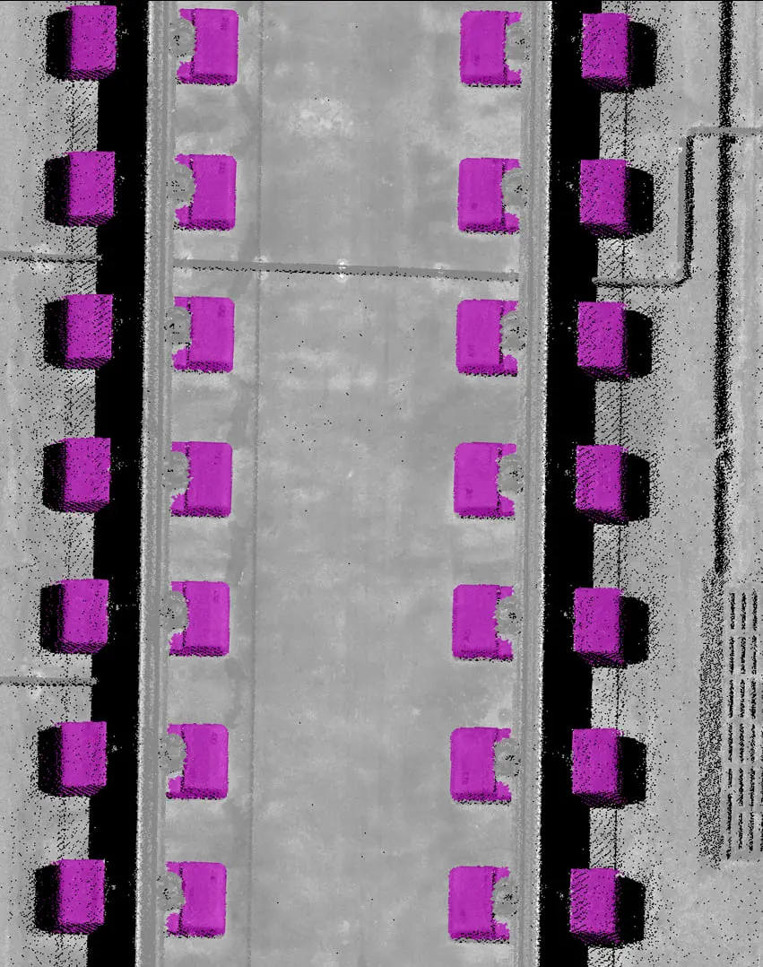Aerial grayscale view of a road or runway flanked by rows of magenta-highlighted rectangular objects, likely vehicles or equipment.